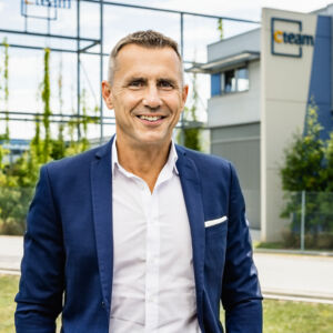 Mann in Anzug lächelt vor Cteam Gebäude, symbolisiert Expertise in Consulting und Anlagenbau.