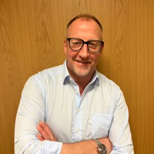 Homem sorrindo, usando óculos e camisa azul, com os braços cruzados. Homem sorrindo, usando óculos e camisa azul, com os braços cruzados.