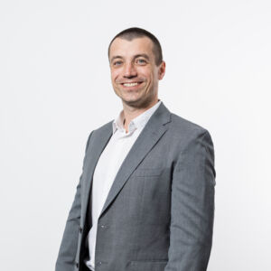 Profissional da Cteam sorrindo, usando terno cinza, em um retrato corporativo com fundo branco. Profissional da Cteam sorrindo, usando terno cinza, em um retrato corporativo com fundo branco.