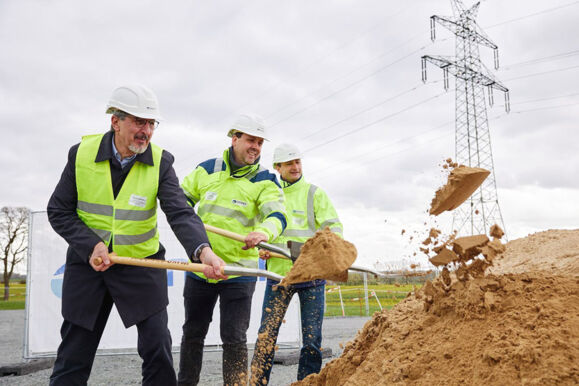 Spatenstich für ein Cteam Infrastrukturprojekt mit Strommasten im Hintergrund.