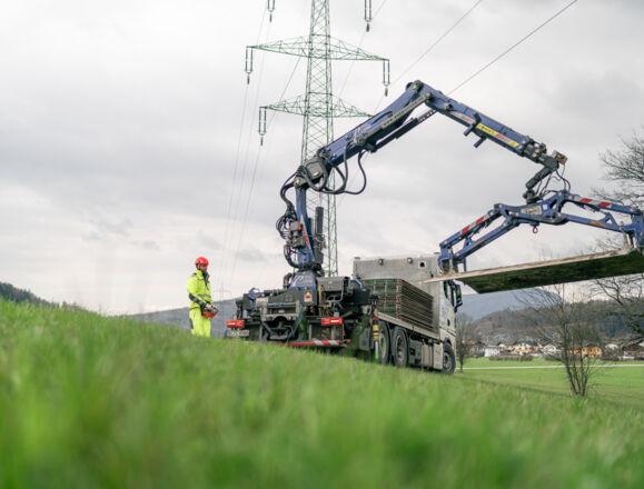 Cteam power line construction work: worker uses crane to install infrastructure near transmission tower. Cteam power line construction work: worker uses crane to install infrastructure near transmission tower.