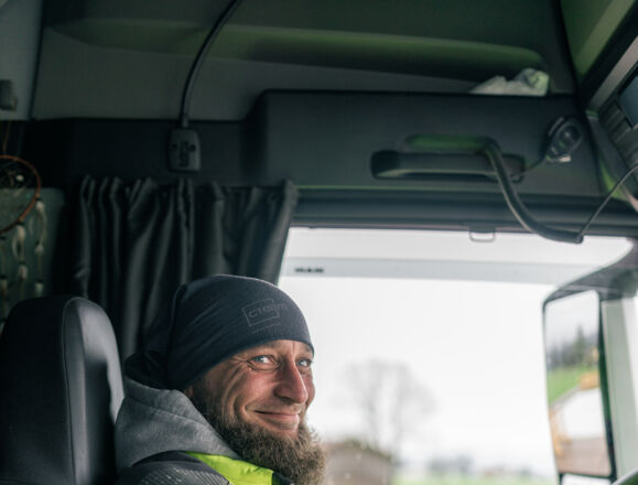 Un chauffeur Cteam souriant, vêtu d'un bonnet, dans la cabine d'un camion.