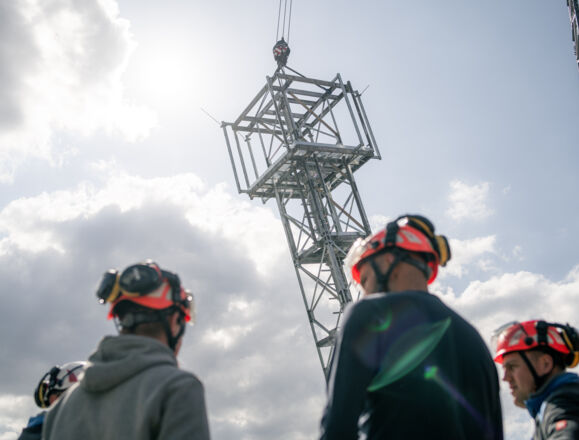 Cteam workers involved in power transmission tower construction, observing a section being lifted by crane. Cteam workers involved in power transmission tower construction, observing a section being lifted by crane.