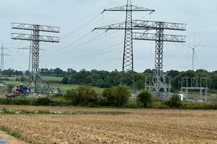 Torres de alta tensão e equipamentos de energia em campo, com guindaste e turbinas eólicas ao fundo, indicando infraestrutura de energia. Torres de alta tensão e equipamentos de energia em campo, com guindaste e turbinas eólicas ao fundo, indicando infraestrutura de energia.